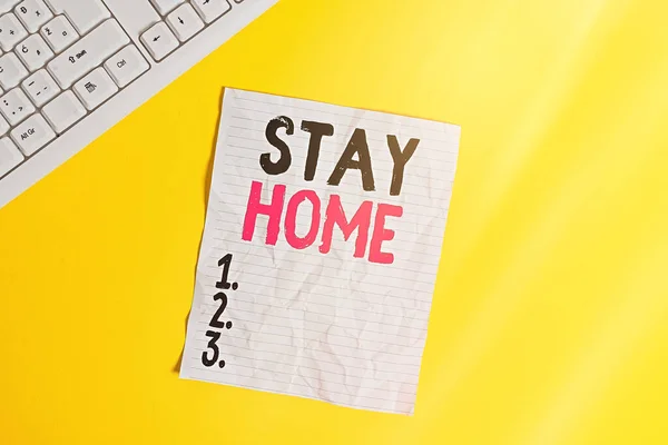 Textskylt "Stanna hemma". Konceptuell bild inte gå ut för en aktivitet och stanna inne i huset eller hemmet Kopiera utrymme på bärbar dator ovan gul bakgrund med st tangentbord på bordet. — Stockfoto