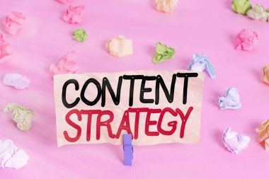 İçerik Stratejisini gösteren bir not yazıyorum. İş fotoğrafı önemli pazarlama yaklaşımı alıcı çekmek için dağıtıldı Renkli buruşuk kağıtlar boş hatırlatıcı pembe zemin çamaşır mandalı.