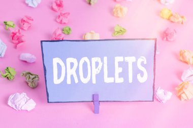 Damlacıkları gösteren bir not yazıyorum. Bir sıvının çok küçük bir damlasını gösteren iş fotoğrafı belirli ıslak yerlerde bulunabilir. Renkli buruşmuş kağıtlar boş hatırlatıcı pembe zemin çamaşır mandalı..