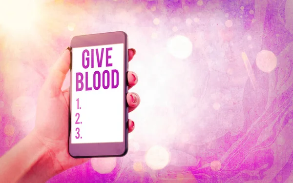Textová značka "Give Blood". Konceptuální fotografie jednotlivce dobrovolně má krev odebraná a používaná pro transfuze Moderní gadgets s bílým displejem obrazovky pod barevným pozadí bokeh. — Stock fotografie