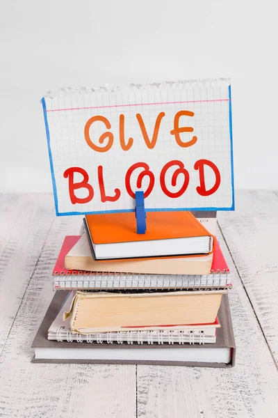 Szöveges jel, ami vért ad. Fogalmi fotó egy egyén önkéntesen vett vért, és használják transzfúzió halom könyvet halom notebook pin ruhacsap színes emlékeztető fehér fa. — Stock Fotó