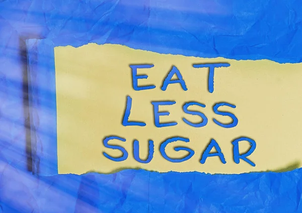 単語の書き込みテキスト以下の砂糖を食べる。砂糖の摂取量を減らし、健康的な食事を豊富に食べるためのビジネスコンセプト木製の古典的なテーブルの背景の上に置かれた裂けた段ボールを転がし. — ストック写真