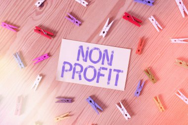 El yazısı Non Profit. Kavram, kar amacı gütmeyen veya yürütülmeyen bir faaliyet anlamına gelir. Renkli çamaşır iğnesi kağıtları boş ahşap zemin ofisini hatırlatır..