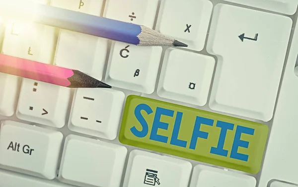 Conceptual hand writing showing Selfie. Business photo text taken by oneself using a digital camera for posting on social network White pc keyboard with empty note paper above white key copy space.