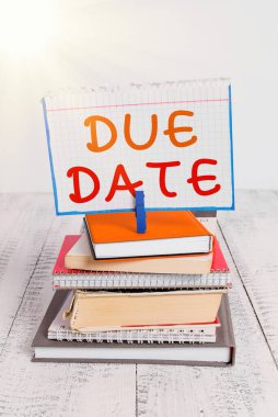 Bitiş Tarihi gösteren metin işareti. Bir şeyin yapılacağı gün ya da tarihte kavramsal fotoğraf veya ödenen yığınla kitap yığını, çamaşır mandalı, hatırlatıcı renkli beyaz ahşap..