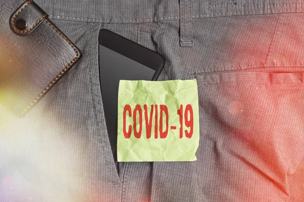 Handwriting text writing Covid19. Concept meaning mild to severe respiratory illness that is caused by a coronavirus Smartphone device inside trousers front pocket with wallet and note paper. — Stock Photo, Image