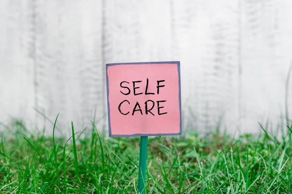 Text sign showing Self Care. Conceptual photo the practice of taking action to preserve or improve one s is health Plain empty paper attached to a stick and placed in the green grassy land. — Stock Photo, Image