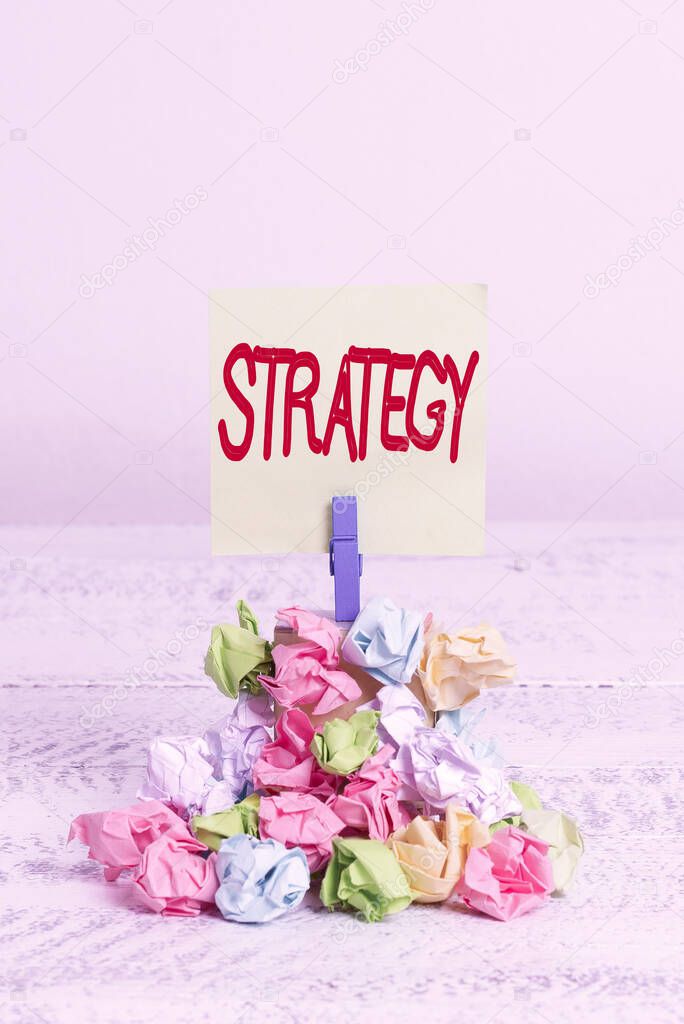 Word writing text Strategy. Business concept for action plan or strategy designed to achieve an overall goal Reminder pile colored crumpled paper clothespin reminder white wooden space.