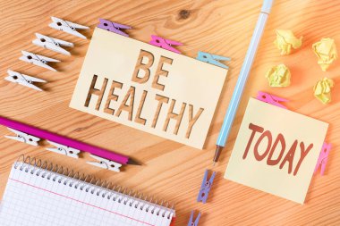 Kelime yazma metni. Sağlıklı ol. Tamamen duygusal ve fiziksel refahın sağlanması için iş konsepti Renkli çamaşır iğnesi kağıtları boş ahşap zemin ofisini anımsatıyor.