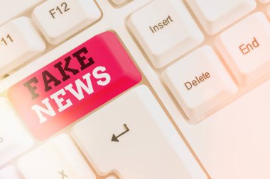 Sahte haberleri gösteren kavramsal el yazısı. İş fotoğrafı metni yanlış bilgi, özgün haber olma kisvesi altında beyaz pc klavye üzerinde beyaz tuş kopya alanı üzerinde boş not kağıdı ile yayınlandı.