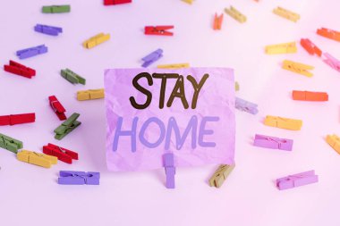 Stay Home 'u gösteren bir not yazıyorum. İş fotoğrafı gösterimi bir etkinlik için dışarı çıkmayın ve evde ya da evde kalın Renkli çamaşır iğnesi kağıtları boş hatırlatıcı beyaz zemin arka plan ofisi.