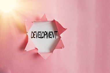 El yazısı Geliştirme. Kavram, birinin ya da bir şeyin büyüdüğü ya da değiştiği bir döngü anlamına gelir. Yırtılmış karton, ahşap bir klasik masa arkaplanının üzerine yerleştirilir..