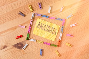 Anemi olduğunu gösteren bir not yazıyorum. İş fotoğraflarında kanda hemoglobin eksikliği görülüyor. Renkli çamaşır iğnesi kağıtları boş ahşap zemin ofisini hatırlatıyor..