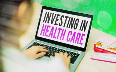 Sağlık Hizmetlerine Yatırım 'ı gösteren bir not yazıyorum. İş fotoğraflarının sergilenmesi, sağlığın bakımına veya iyileştirilmesine para yatırdı. Modern cihazlar renkli bokeh arkaplan altında beyaz ekran.