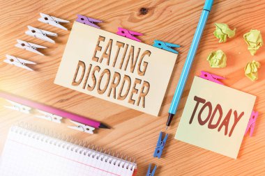 Metin yazma, yeme bozukluğu. Hastalıklar için iş kavramı ya da yeme alışkanlıklarında ciddi rahatsızlıklar. Renkli çamaşır iğnesi kağıtları boş ahşap zemin ofisini anımsatıyor..