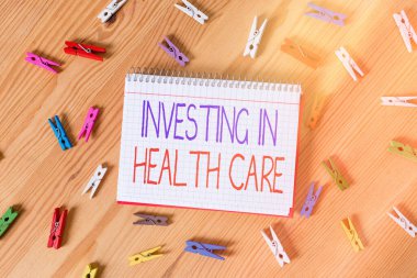 Sağlık hizmetlerine yatırım yapıldığını gösteren kavramsal el yazısı. İş fotoğrafı metni, sağlığın bakımına veya iyileştirilmesine para yatırdı Renkli buruşuk kağıtlar ahşap zemin çamaşır mandalı.