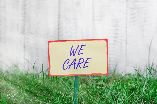 Writing note showing We Care. Business photo showcasing Cherishing someones life Giving care and providing their needs Plain paper attached to stick and placed in the grassy land.