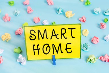 Smart Home 'a mesaj yazıyorum. Donanımlı ev için iş konsepti telefon veya bilgisayar ile uzaktan kontrol edilebilir. Renkli buruşuk kağıtlar boş hatırlatıcı mavi zemin çamaşır mandalı.