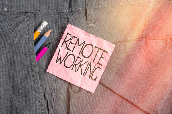 Tekstbord met Remote Working. Conceptuele foto stijl die professionals in staat stelt om buiten een kantoor te werken Schrijfapparatuur en roze notitie papier in zak van man werk broek. — Stockfoto