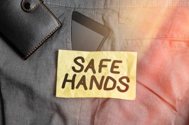 Güvenli Eller 'i gösteren bir not yazıyorum. İş fotoğrafı gösterimi. Dezenfekte için ellerin sterilitesi ve temizliği sağlanıyor. Pantolonun ön cebinde cüzdanı olan akıllı telefon cihazı..