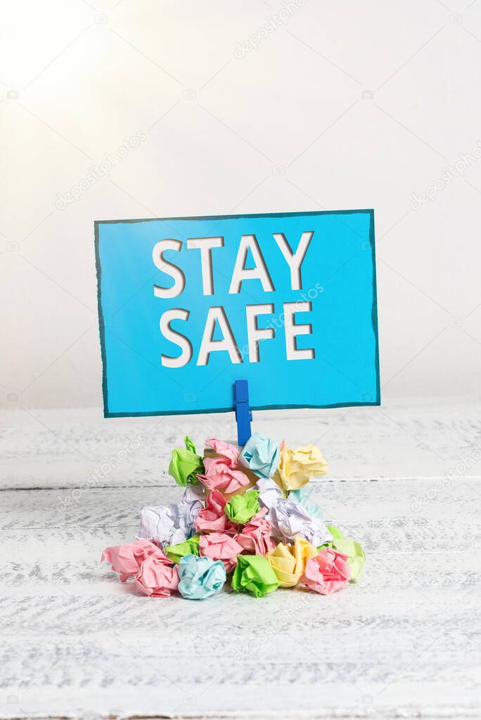 Text sign showing Stay Safe. Conceptual photo secure from threat of danger, harm or place to keep articles Reminder pile colored crumpled paper clothespin reminder white wooden space.