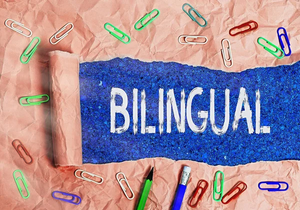 Text sign showing Bilingual. Conceptual photo using or able to use two languages especially with equal fluency Rolled ripped torn cardboard placed above a wooden classic table backdrop.