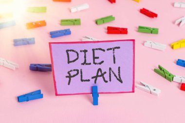 Diyet Planı 'nı gösteren bir not yazıyorum. Belirli bir kilo elde etmek için iş fotoğraflarının gösterilmesi planlanıyor. Renkli çamaşır iğnesi kağıtları boş, pembe ofis broşu..