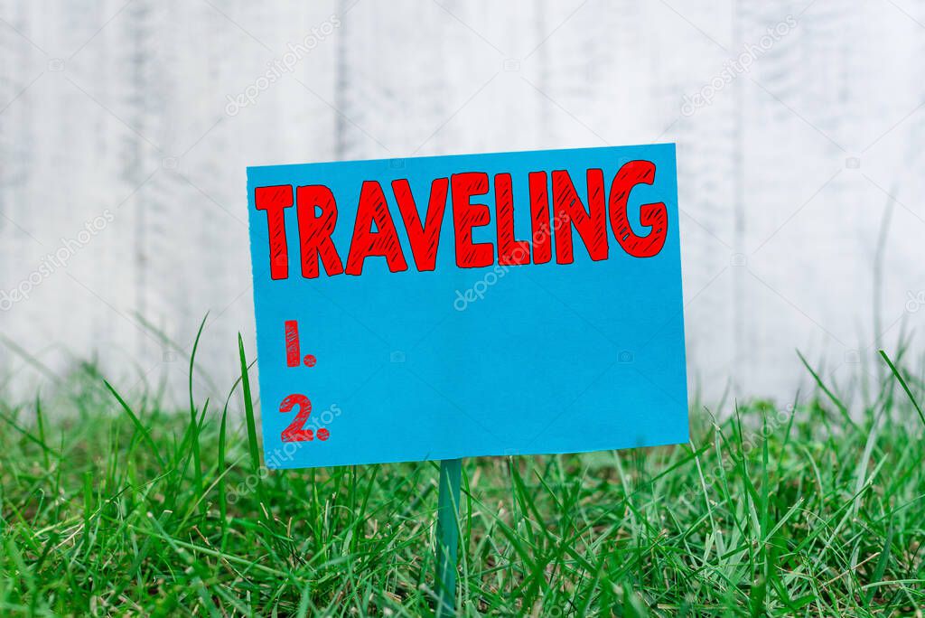 Handwriting text Traveling. Concept meaning going to different places instead of staying in one place Plain empty paper attached to a stick and placed in the green grassy land.