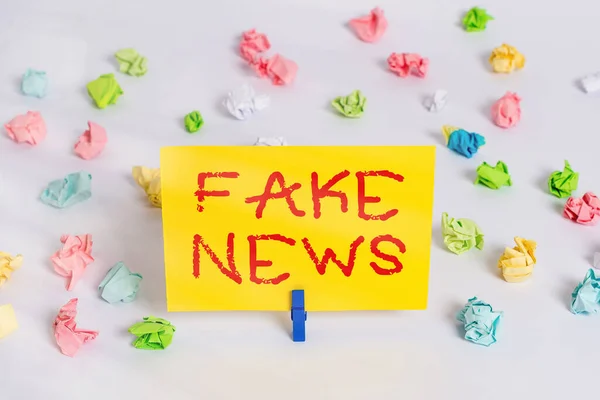 Texto de escritura Fake News. Concepto que significa información falsa publicar bajo el pretexto de ser noticias auténticas Papeles arrugados coloreados recordatorio vacío piso blanco tendedero . — Foto de Stock