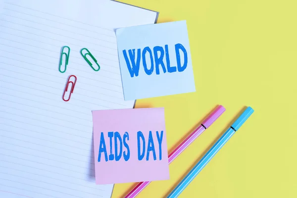 Handstilstext Världsaidsdagen. Begreppet innebär en internationell dag för att öka medvetenheten om AIDS pandemi Tom blått papper med kopia utrymme gem och pennor på det gula bordet. — Stockfoto