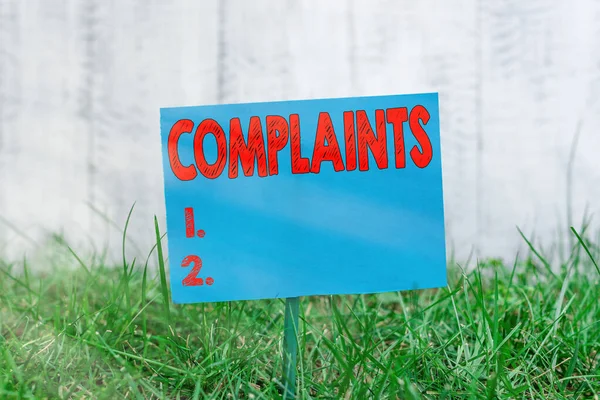 Handwriting text Complaints. Concept meaning something that is the cause or subject of protest or outcry Plain empty paper attached to a stick and placed in the green grassy land. — Stock Photo, Image