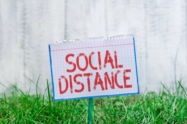Текст слова Social Distance. Бизнес-концепция для степени принятия общего взаимодействия физических лиц Математическая бумага прикреплена к палочке и помещена в зеленую травянистую землю. — стоковое фото