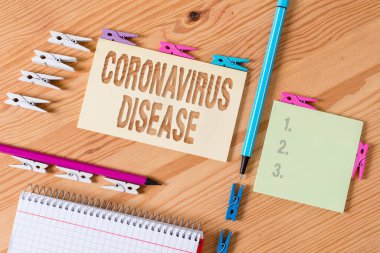 Coronavirus Hastalığı 'nı gösteren bir not yazıyorum. İş fotoğrafı sergisi, yeni bir virüs olan SARSCoV2 'nin sebep olduğu hastalık olarak tanımlanıyor. Renkli çamaşır iğnesi kağıtları boş ahşap zemin ofisini hatırlatıyor..