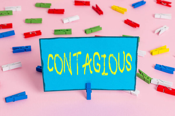 Text sign showing Contagious. Conceptual photo transmissible by direct or indirect contact with infected an individual Colored clothespin papers empty reminder pink floor background office pin.