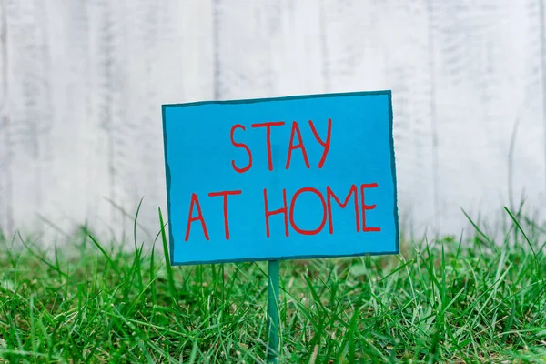 Scrittura concettuale a mano che mostra Stay At Home. Foto aziendale che mostra il controllo del movimento che impedisce agli individui di essere esposti pubblicamente Carta normale attaccata al bastone e posta nell'erboso — Foto Stock