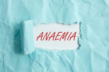 Anemi belirtileri var. Kavramsal fotoğraf, kanda hemoglobin eksikliğiyle işaretlenmiş yırtılmış karton, ahşap bir masa arkaplanının üzerine yerleştirilmiş..