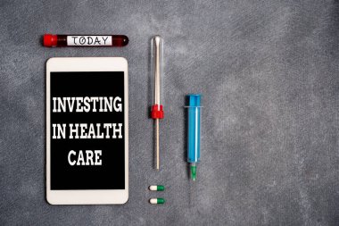 Sağlık hizmetlerine yatırım yapıldığını gösteren kavramsal el yazısı. İş fotoğraflarının sergilenmesi, sağlık hizmetleri veya kan örneği şişesi tıbbi aksesuarlarının geliştirilmesine para yatırdı..