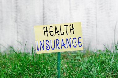 Kelime yazma Sağlık Sigortası. Bir çubuğa bağlanmış ve yeşil çimenli araziye yerleştirilmiş sigortalı boş kağıdın tıbbi giderlerini karşılama amaçlı iş konsepti.