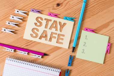 Stay Safe 'i gösteren bir not yazıyorum. İş fotoğrafı sergisi tehlike, zarar veya makaleleri saklamak için güvenli bir yer Renkli çamaşır iğnesi kağıtları boş ahşap zemin ofisini anımsatıyor.