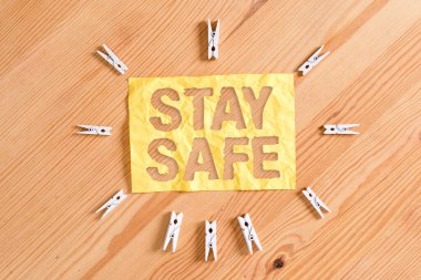 Stay Safe 'i gösteren bir not yazıyorum. İş fotoğrafı sergisi tehlike, zarar veya makaleleri saklamak için güvenli bir yer Renkli çamaşır iğnesi kağıtları boş ahşap zemin ofisini anımsatıyor.