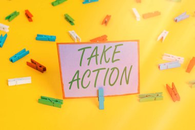 Take Action 'ı gösteren bir not yazıyorum. Özel bir sonuç elde etmek için bir şey yapmak ya da hareket etmek için iş fotoğrafı sergisi Renkli çamaşır iğnesi kağıtları boş hatırlatıcı sarı zemin arka plan ofisi.
