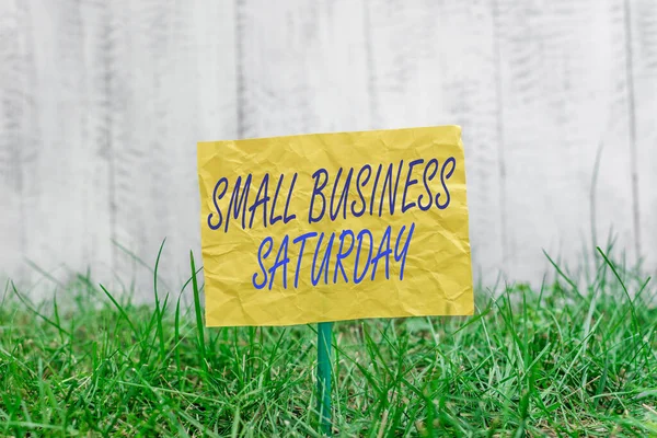 Texto para escrita de palavras Small Business Saturday. Conceito de negócio para férias de compras americanas realizadas durante o sábado Papel vazio liso anexado a um pau e colocado na terra verde gramado. — Fotografia de Stock