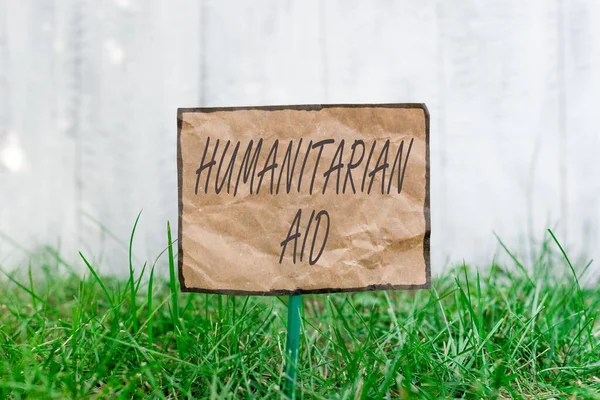 Handwriting text writing Humanitarian Aid. Concept meaning immediate assistance provided after natural and manmade disaster Crumpled paper attached to a stick and placed in the green grassy land. — Stock Photo, Image