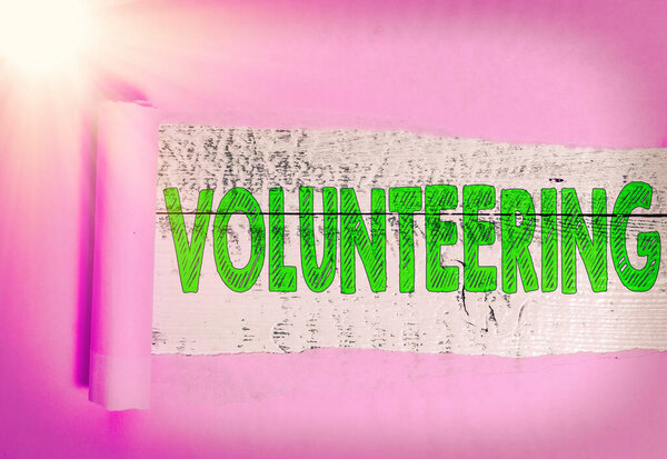 Text sign showing Volunteering. Conceptual photo an individual who voluntarily expresses a willingness to undertake Rolled ripped torn cardboard placed above a wooden classic table backdrop.