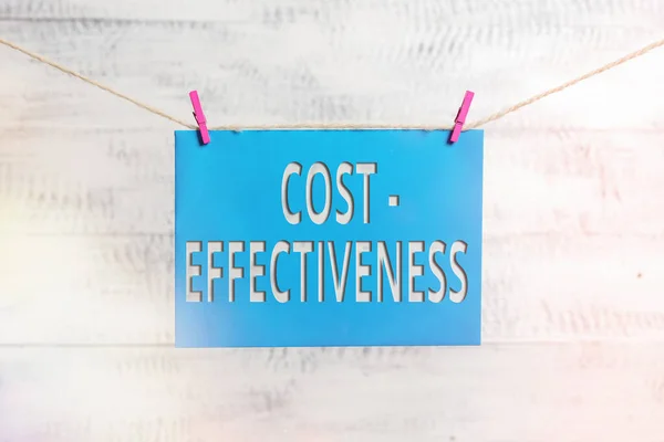 Handwriting text Cost Effectiveness. Concept meaning degree to which something is effective in relation to its cost. Clothesline clothespin rectangle shaped paper reminder white wood desk.