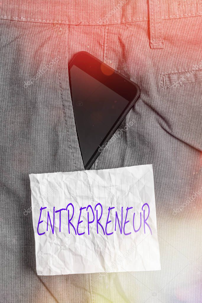 Text sign showing Entrepreneur. Conceptual photo one who organizes and assumes the risks of a business Smartphone device inside formal work trousers front pocket near note paper.