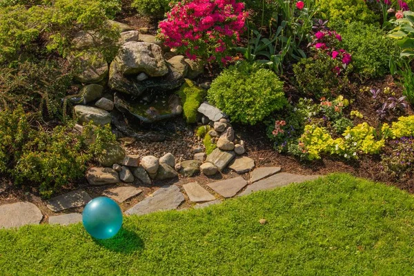 Backyard garden stone fountain design with bright turquoise blue childhood toy ball in spring sunlight