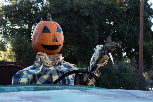 Close-up of smiling, happy, welcoming, fun friendly pumpkin head scarecrow driving an old truck to a halloween harvest party