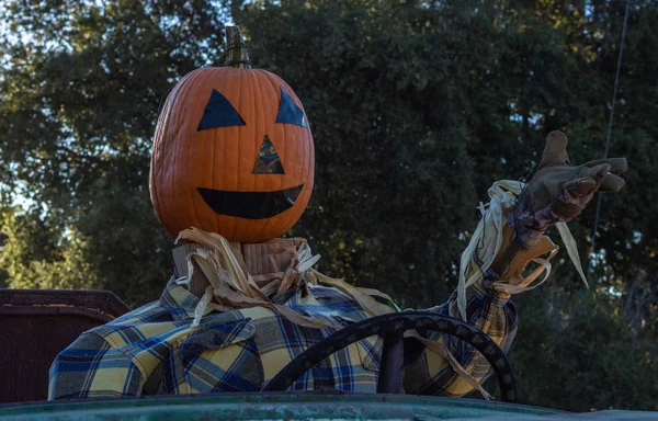 Close-up of smiling, happy, welcoming, fun friendly pumpkin head scarecrow driving an old truck to a halloween harvest party