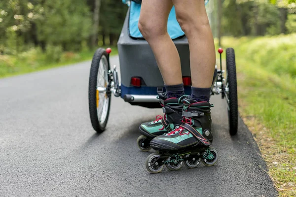 ベビーカーで屋外スケートでラインスケートの若いフィット母の女性 — ストック写真